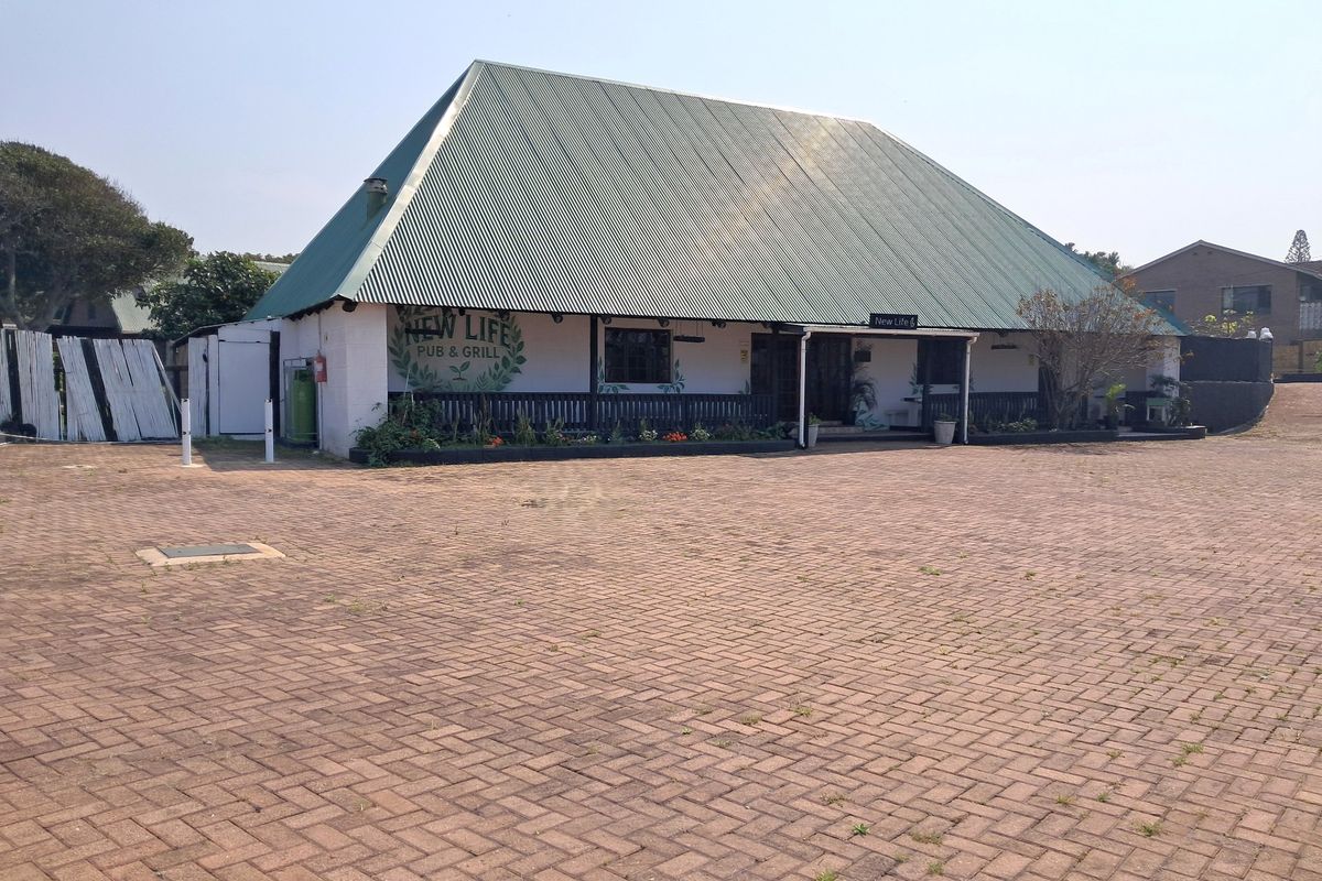 Front view of a commercial pub and grill building featuring a large corrugated metal roof, covered veranda, and extensive paved parking area.