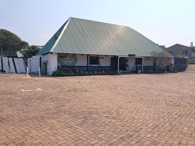 Front view of a commercial pub and grill building featuring a large corrugated metal roof, covered veranda, and extensive paved parking area.