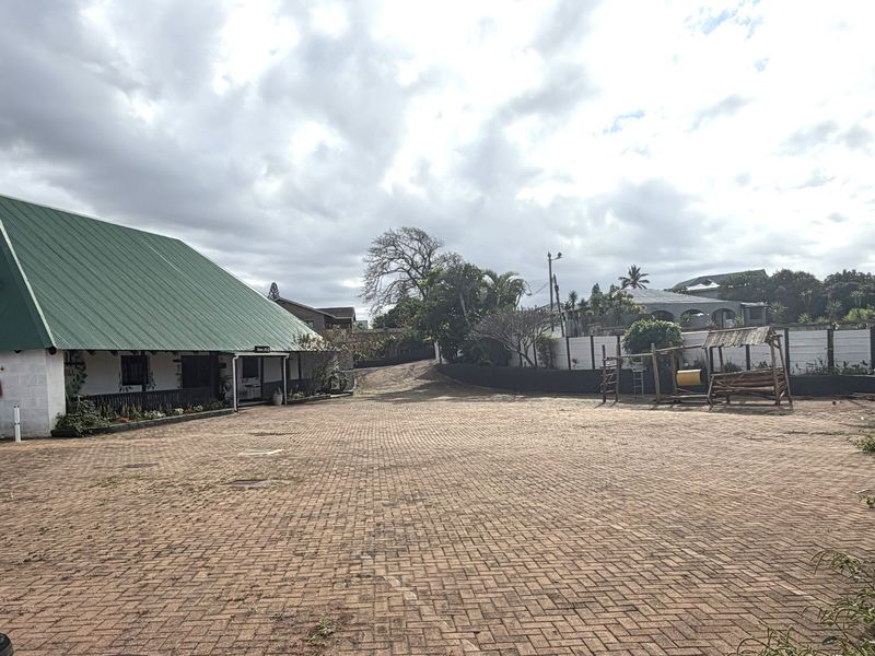 Spacious paved outdoor area featuring a building with a pitched green metal roof and a covered patio section.