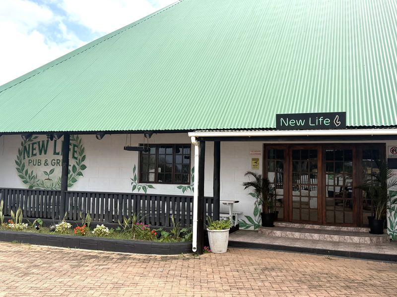 Front facade of a commercial pub and grill featuring a prominent green corrugated metal roof, timber-framed entrance doors, and a paved exterior area.