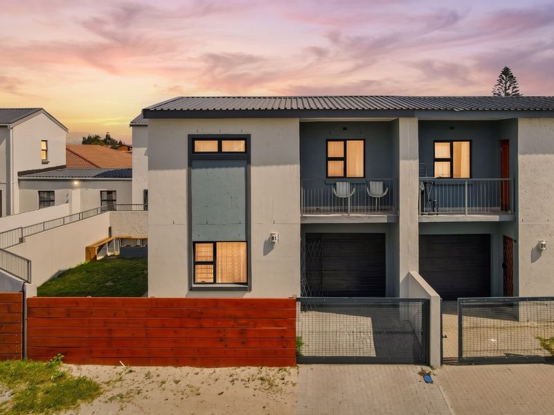 A modern two-story townhouse exterior featuring a metal roof, private balcony, integrated garage, and secure perimeter fencing at sunset.