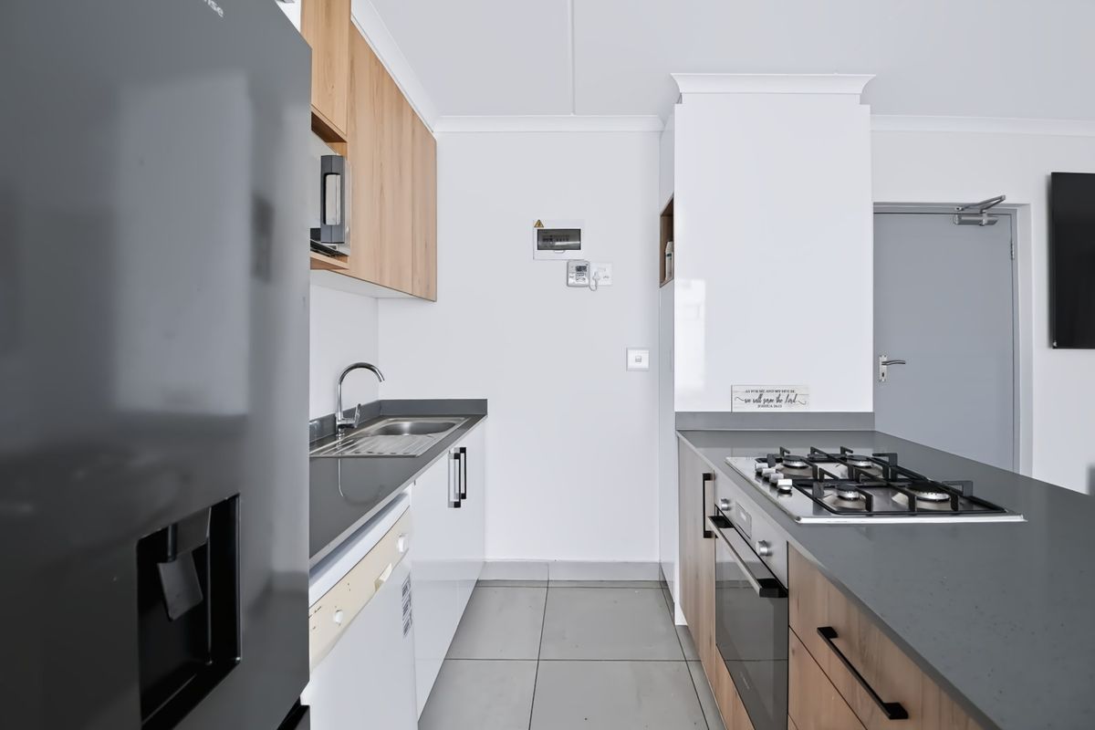 Modern kitchen featuring sleek cabinetry, stone countertops, a gas hob, built-in oven, and tiled flooring in a clean, contemporary layout.
