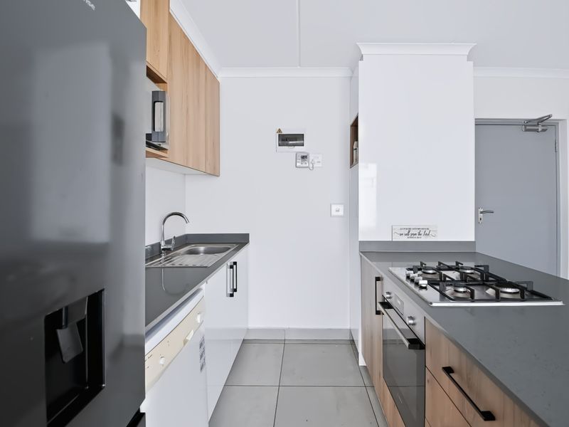 Modern kitchen featuring sleek cabinetry, stone countertops, a gas hob, built-in oven, and tiled flooring in a clean, contemporary layout.