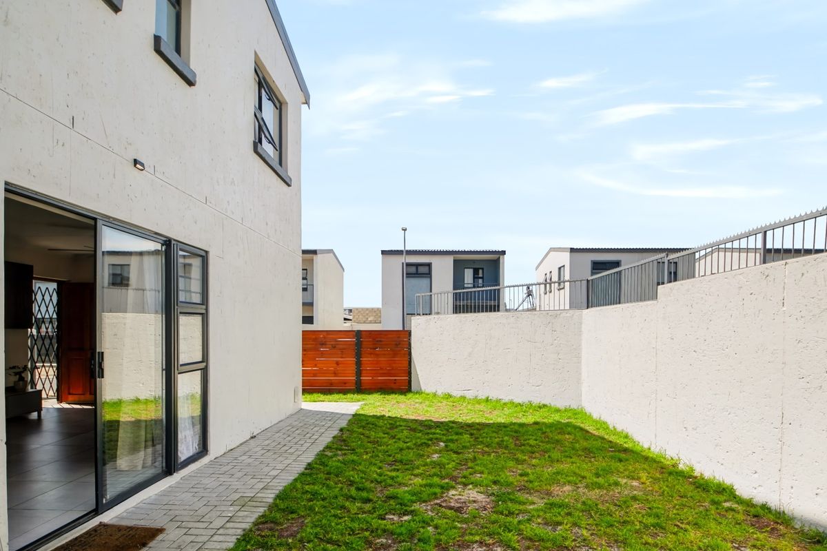 A private rear garden featuring a paved walkway, a small lawn, and a secure boundary wall with metal fencing.