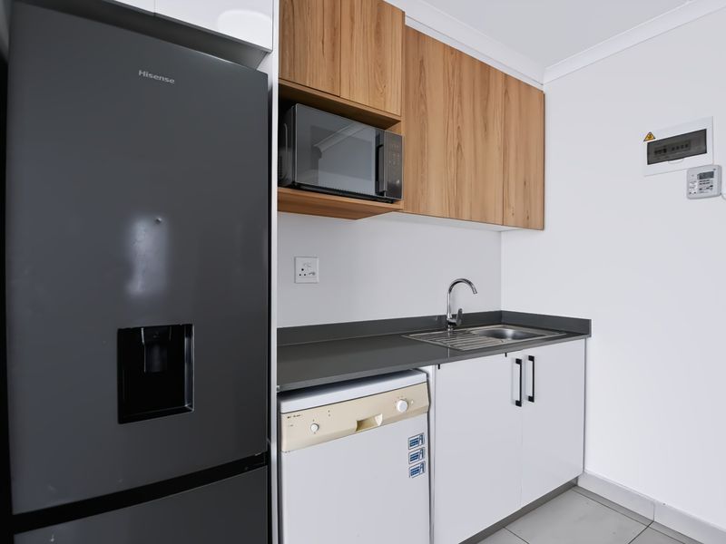 A compact, modern scullery featuring wood-finish upper cabinets, white lower cabinetry, stone countertops, a stainless steel sink, and a built-in microwave.