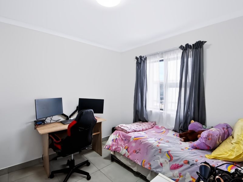 A well-lit bedroom featuring neutral wall finishes, tiled flooring, and a built-in wardrobe, providing a functional and comfortable living space.
