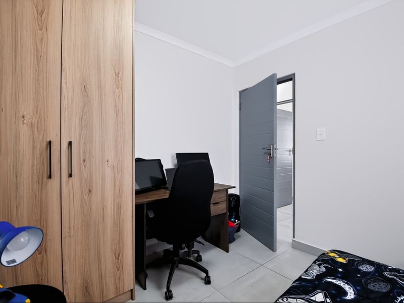 A functional bedroom featuring light-toned built-in wardrobes, neutral wall finishes, and tiled flooring, providing a clean and modern living space.