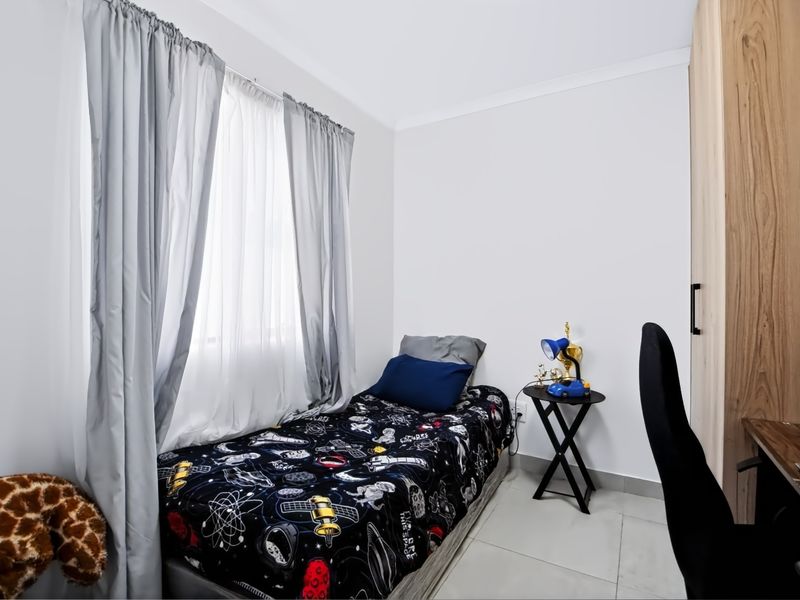 A well-maintained bedroom featuring neutral tiled flooring, a built-in wardrobe, and large windows with installed curtain tracks.