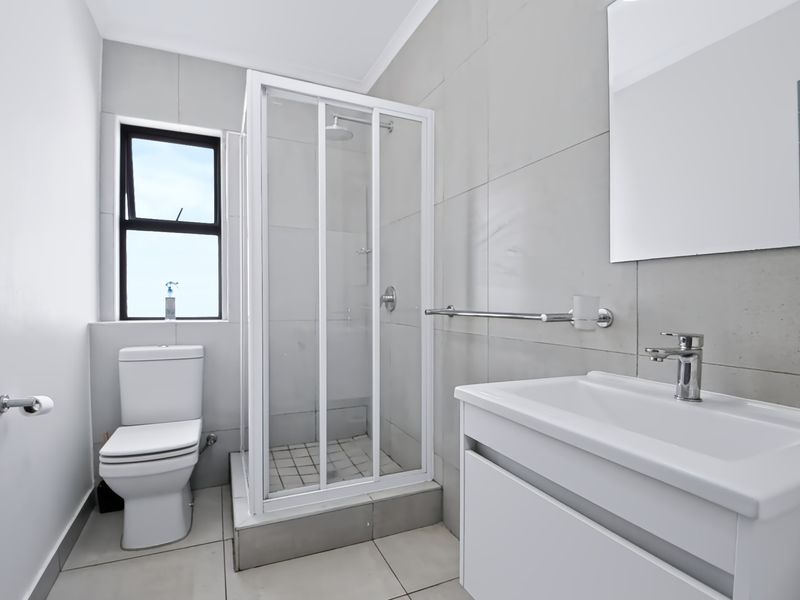 A clean, modern bathroom featuring a glass shower enclosure, a white vanity with basin, and neutral wall and floor tiling.