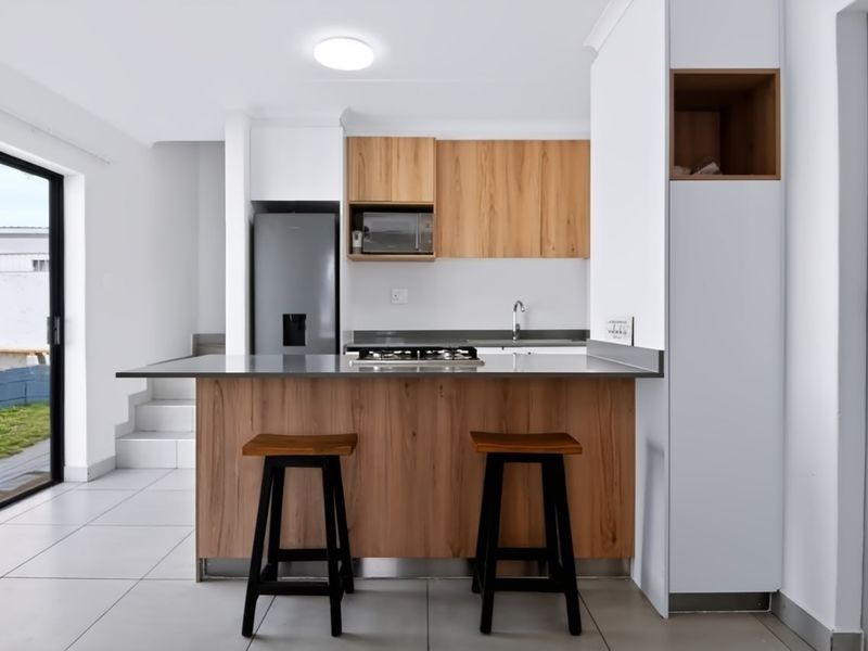 Modern kitchen featuring wood-finish cabinetry, stainless steel countertops, a gas hob, and direct access to the outdoor area through a sliding glass door.