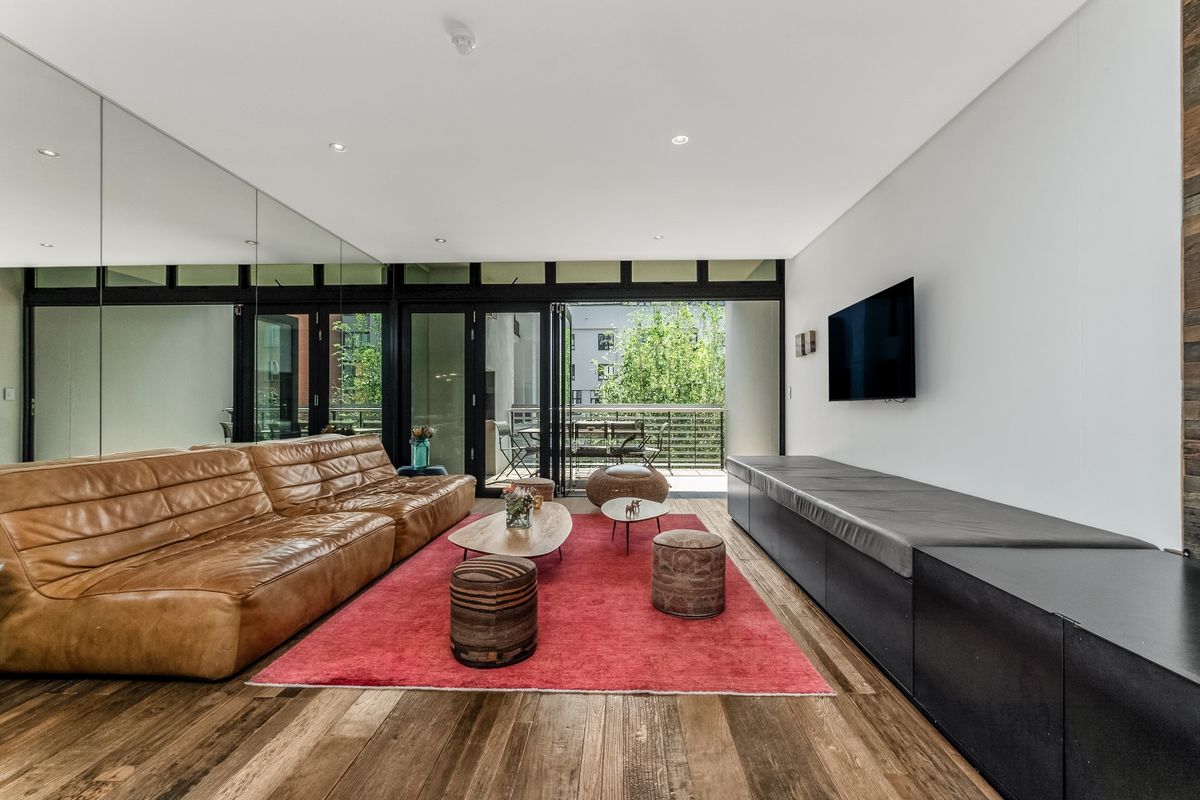 Modern living room featuring hardwood flooring, a large mirrored wall, built-in media cabinetry, and bi-fold doors opening to a private balcony.