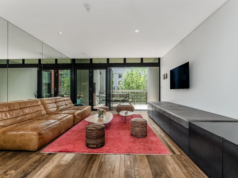 Modern living room featuring hardwood flooring, a large mirrored wall, built-in media cabinetry, and bi-fold doors opening to a private balcony.