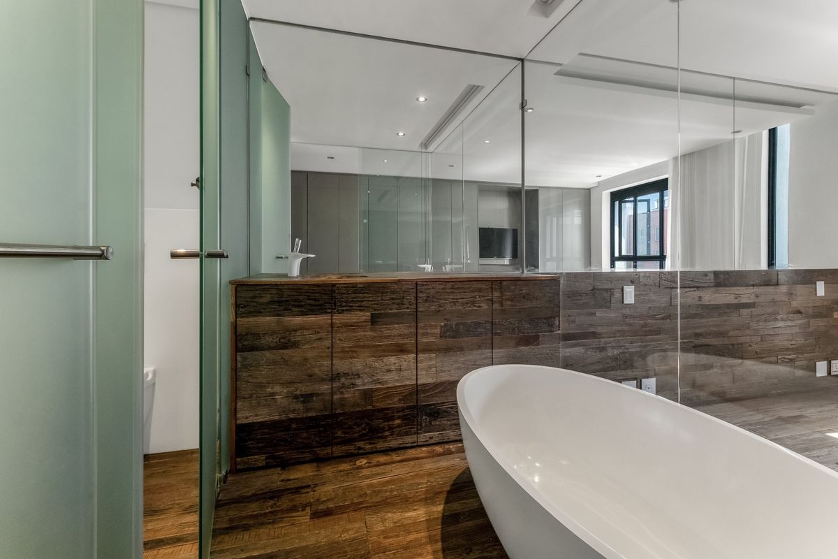 Modern bathroom featuring a sleek freestanding bathtub, wood-paneled vanity, and glass partitions, creating a contemporary and sophisticated aesthetic.