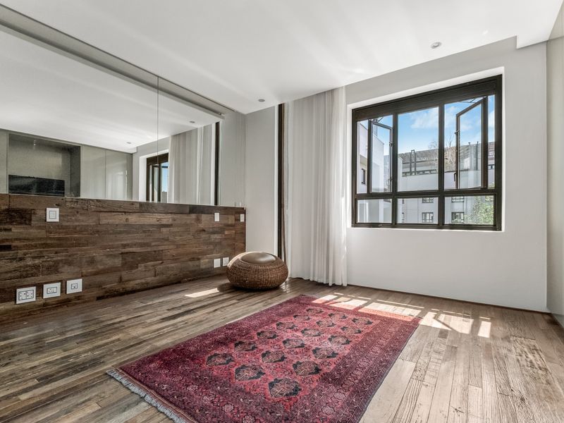 A bright bedroom featuring timber flooring, a feature timber wall with integrated mirror, and large casement windows allowing for ample natural light.