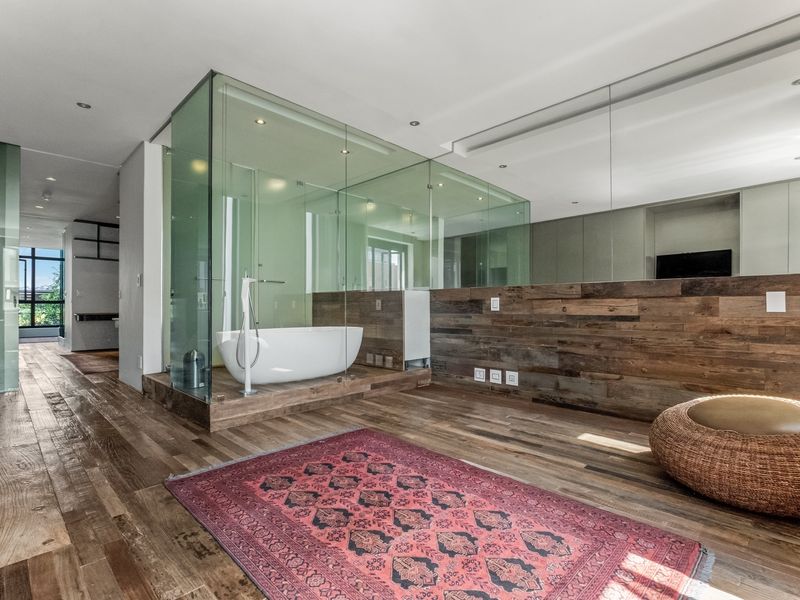 Modern bedroom suite featuring an open-plan glass-enclosed bathroom, freestanding bathtub, timber wall accents, and high-quality hardwood flooring.