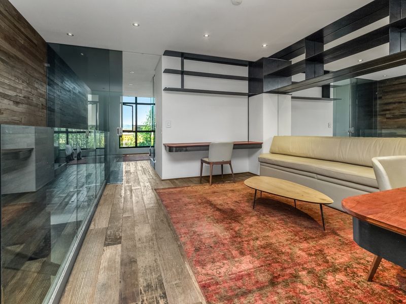 Modern living area featuring hardwood flooring, recessed lighting, a sleek glass partition, and custom built-in shelving and desk space.
