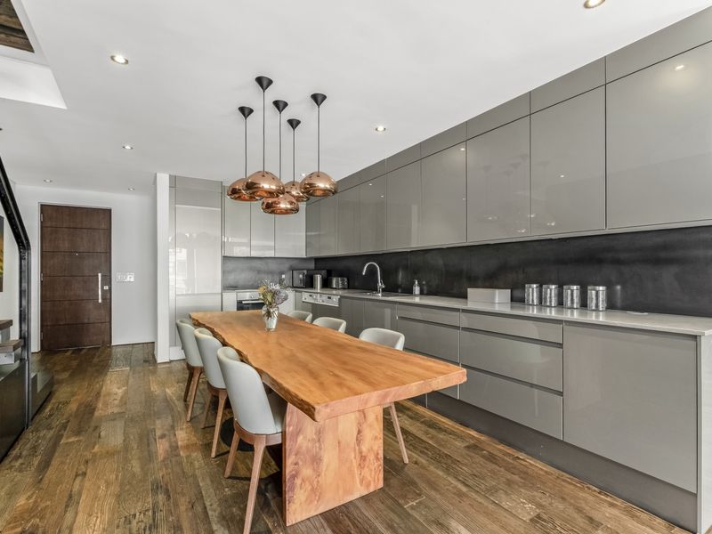 Modern open-plan kitchen featuring sleek grey cabinetry, dark stone splashback, integrated appliances, and warm hardwood flooring, seamlessly flowing into the dining area.