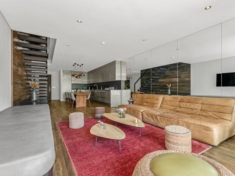 Modern open-plan living area featuring hardwood floors, a sleek kitchen with integrated cabinetry, a feature timber wall, and a striking staircase.