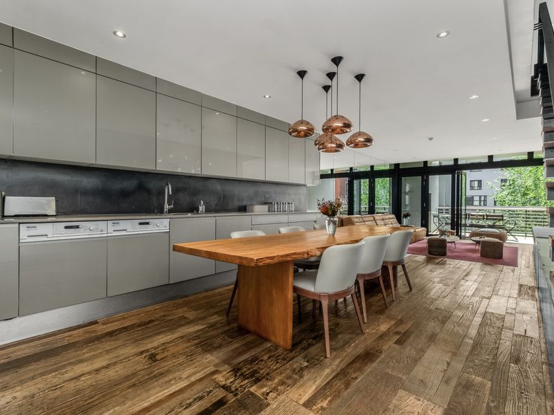 Modern open-plan living area featuring high-gloss cabinetry, integrated appliances, hardwood flooring, and a seamless transition to the outdoor balcony space.