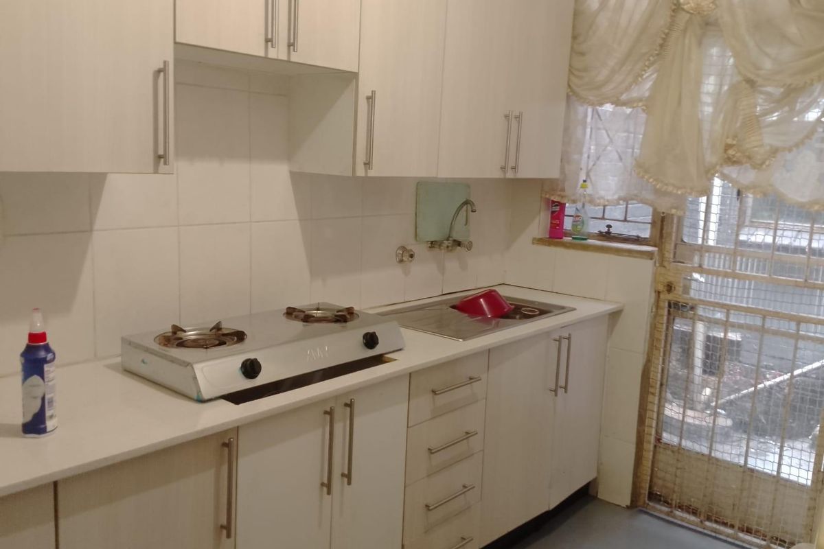 A functional kitchen featuring white built-in cabinetry, a gas hob, stainless steel sink, and tiled backsplash with direct access to a secure exterior area.