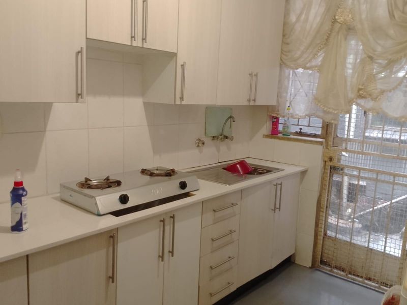 A functional kitchen featuring white built-in cabinetry, a gas hob, stainless steel sink, and tiled backsplash with direct access to a secure exterior area.