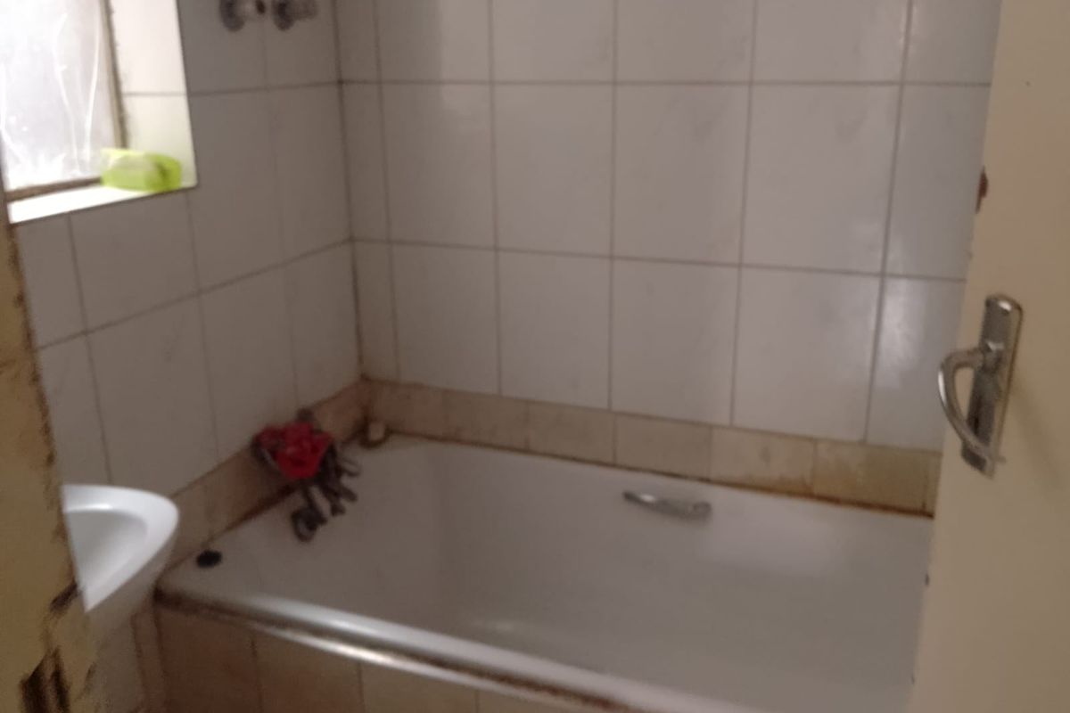 A dated bathroom featuring a standard bathtub and basin with tiled walls, requiring renovation to update the finishes and fixtures.