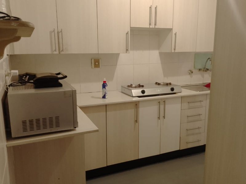 A functional kitchen featuring white built-in cabinetry, a gas hob, and a stainless steel sink with a tiled backsplash.