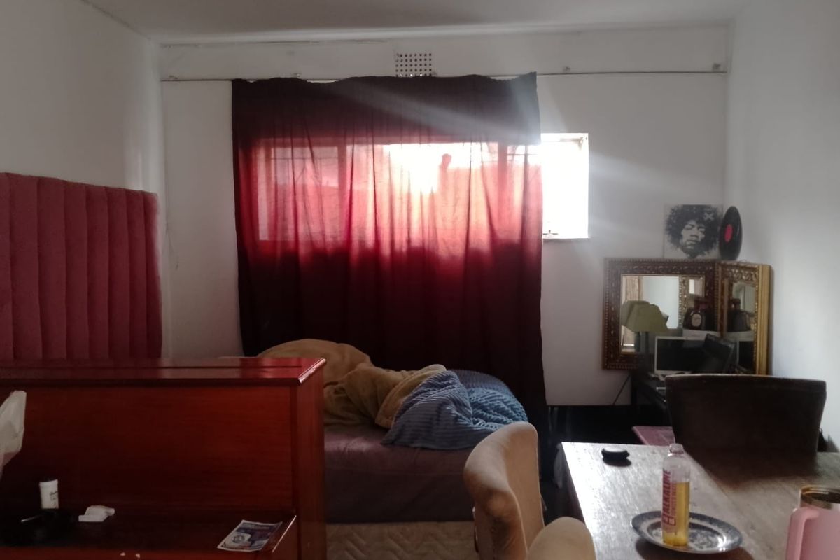 A bedroom space featuring a window with curtain treatments and a ventilation grille, requiring cosmetic updates to improve the overall aesthetic.