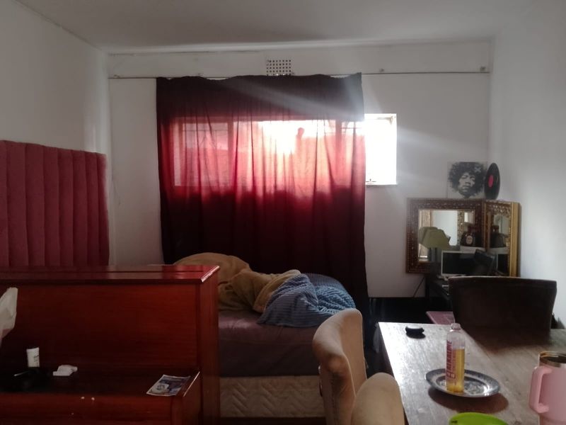 A bedroom space featuring a window with curtain treatments and a ventilation grille, requiring cosmetic updates to improve the overall aesthetic.