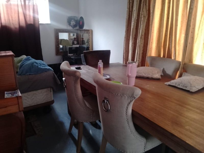 A dining area featuring a large wooden table and upholstered chairs, with natural light entering through window treatments.