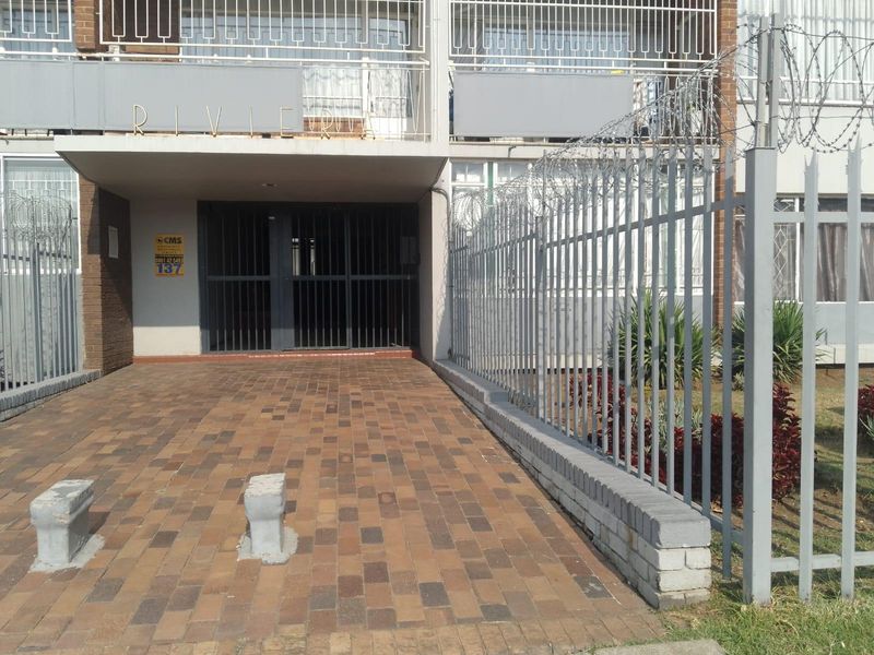 Front entrance of the apartment building featuring a paved driveway, secure gated access, and perimeter security fencing with razor wire.