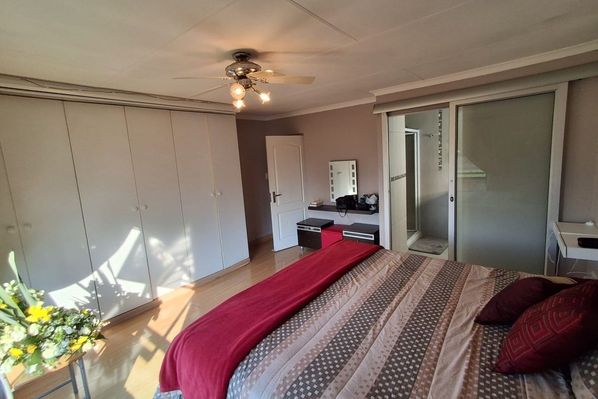 Spacious bedroom featuring laminate flooring, extensive built-in cupboards, a ceiling fan, and direct access to an en-suite bathroom through a sliding door.
