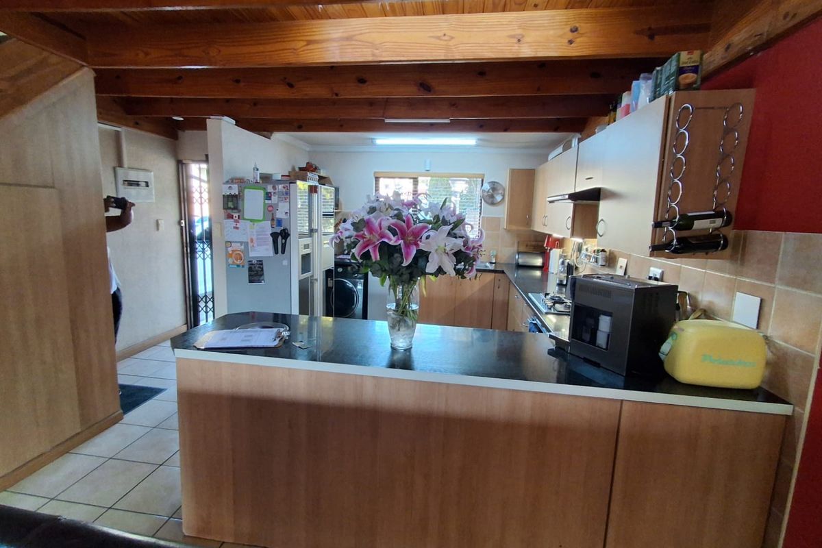 A functional kitchen featuring warm timber ceiling beams, laminate cabinetry, and a breakfast bar, offering a practical layout with integrated cooking appliances.