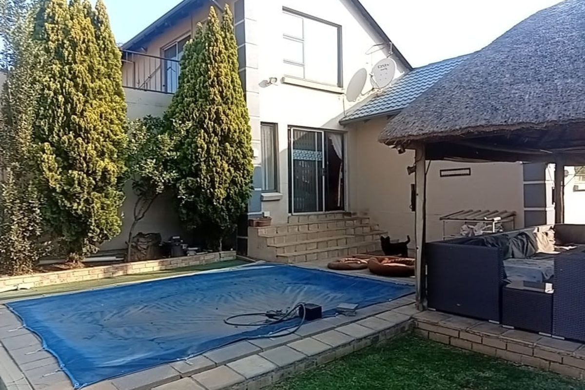 Rear exterior view featuring a swimming pool with cover, a thatched lapa entertainment area, and a multi-story house facade with a balcony.