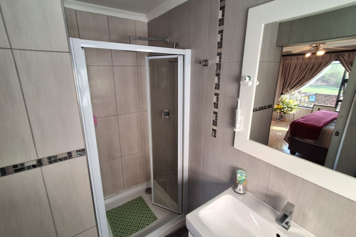 A functional bathroom featuring a glass-enclosed shower, a modern vanity basin with a mixer tap, and neutral wall tiling.