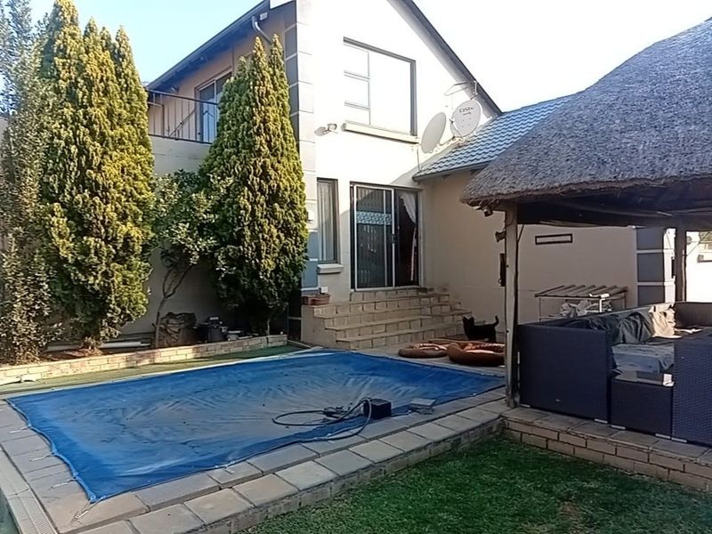 Rear exterior view featuring a swimming pool with cover, a thatched lapa entertainment area, and a multi-story house facade with a balcony.