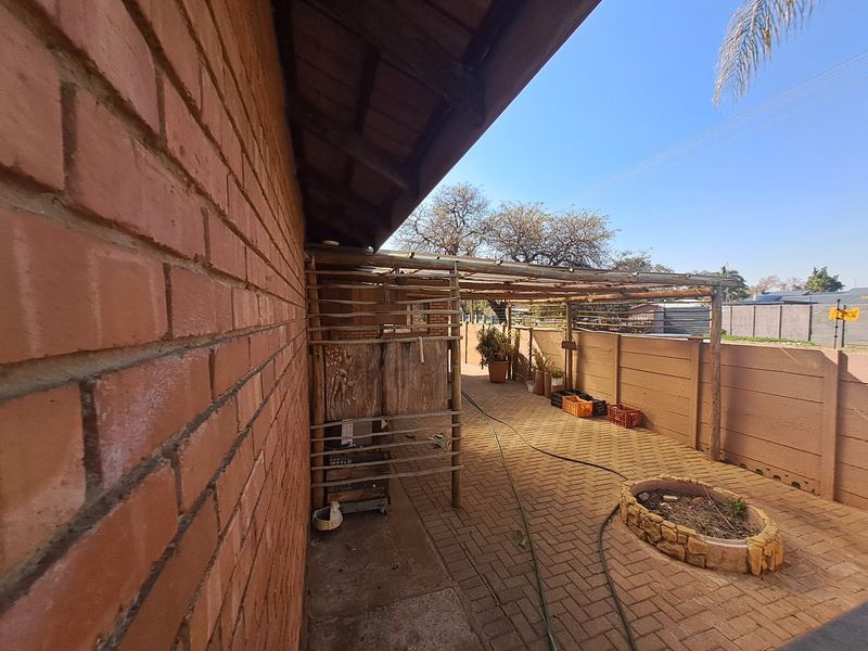 Rear exterior area featuring a paved patio, timber pergola structure, and a raised stone planter against a brick house facade.