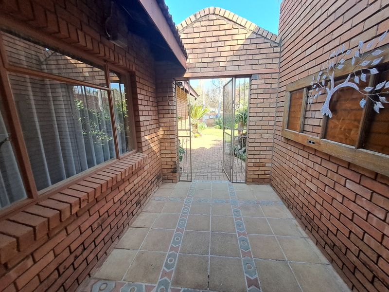 A covered outdoor patio area featuring exposed brickwork, decorative tiled flooring, and a metal security gate leading to the garden.