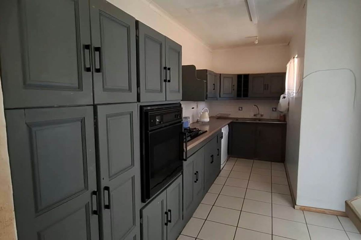 A functional kitchen featuring dark grey cabinetry, a built-in oven, gas hob, and tiled flooring, requiring some cosmetic updates and electrical tidying.