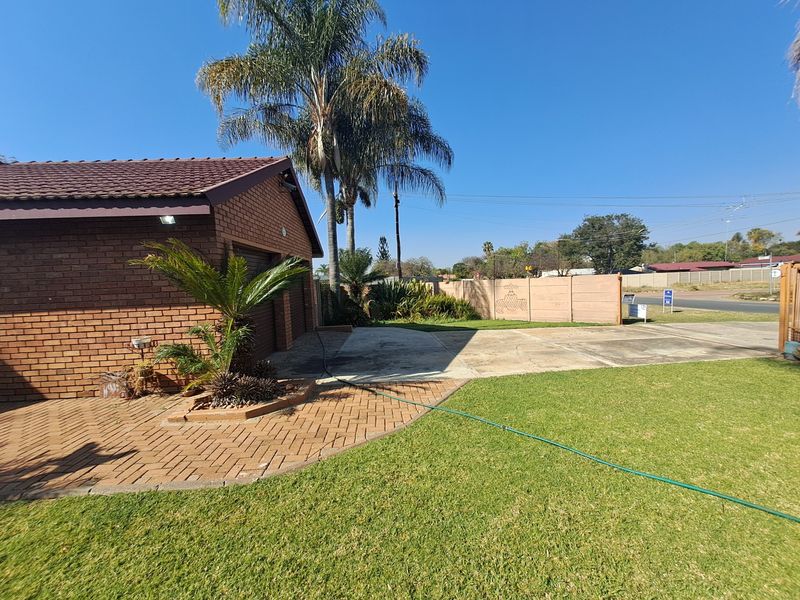 Front exterior view of the property featuring a brick garage, paved driveway, and a well-maintained lawn with boundary walling.