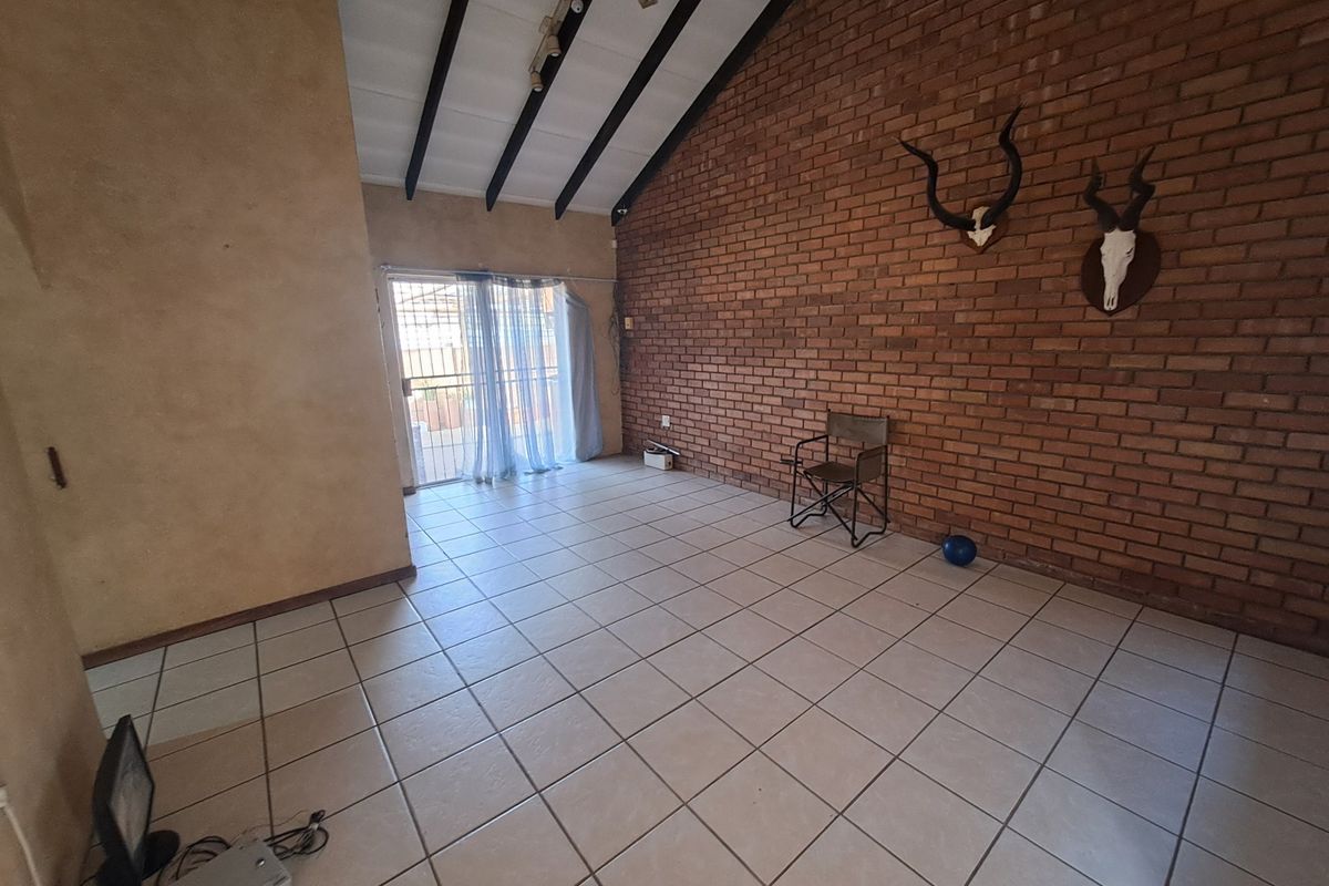 Spacious living area featuring a high vaulted ceiling with exposed timber beams, a prominent brick feature wall, and neutral ceramic floor tiles.