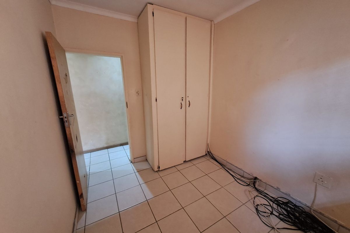 A vacant bedroom featuring tiled flooring, a built-in wardrobe, and coving, requiring cosmetic updates and cable management.