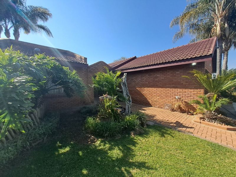 A well-maintained face brick house exterior featuring a tiled roof, paved entrance walkway, and established garden landscaping under a clear blue sky.