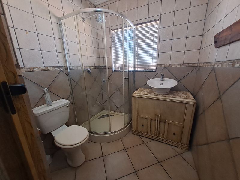 A functional bathroom featuring a corner shower enclosure, a vanity cabinet with a vessel basin, and tiled wall and floor finishes.