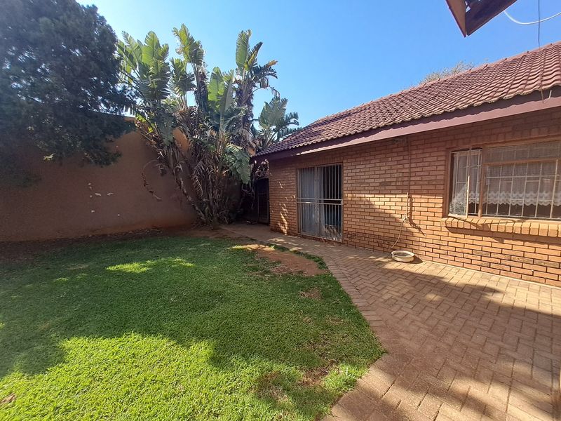 Rear exterior view of the house featuring a brick facade, tiled roof, paved patio area, and a private garden space.