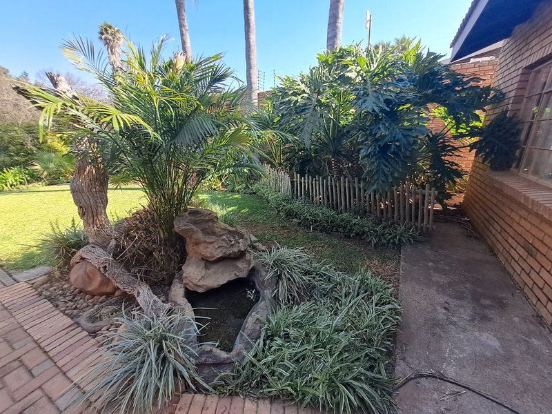 A landscaped garden area featuring a small water feature, brick paving, a concrete pathway, and established greenery alongside a brick exterior wall.