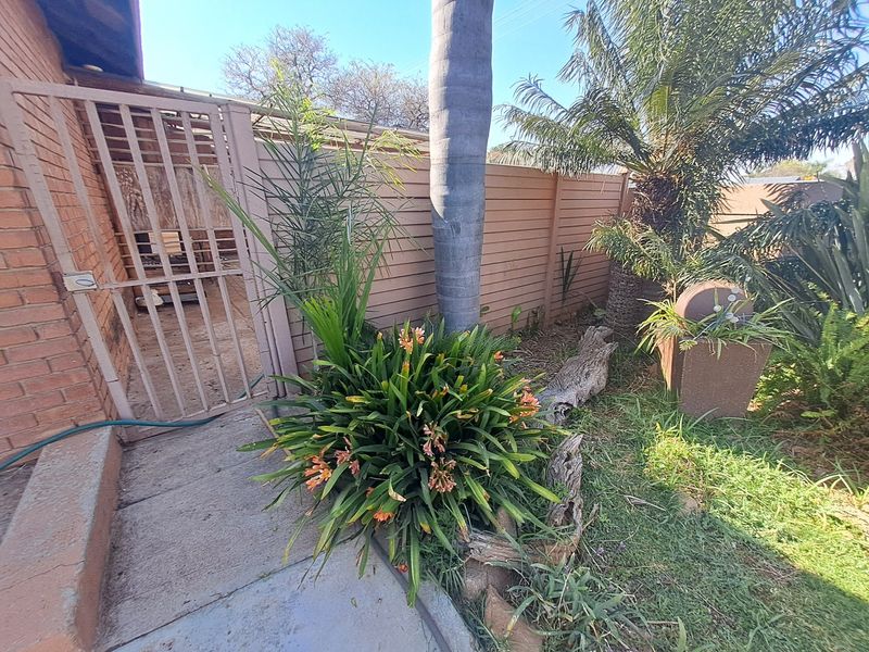 A view of the rear garden area featuring a brick wall, a metal security gate, and established landscaping with a timber boundary fence.