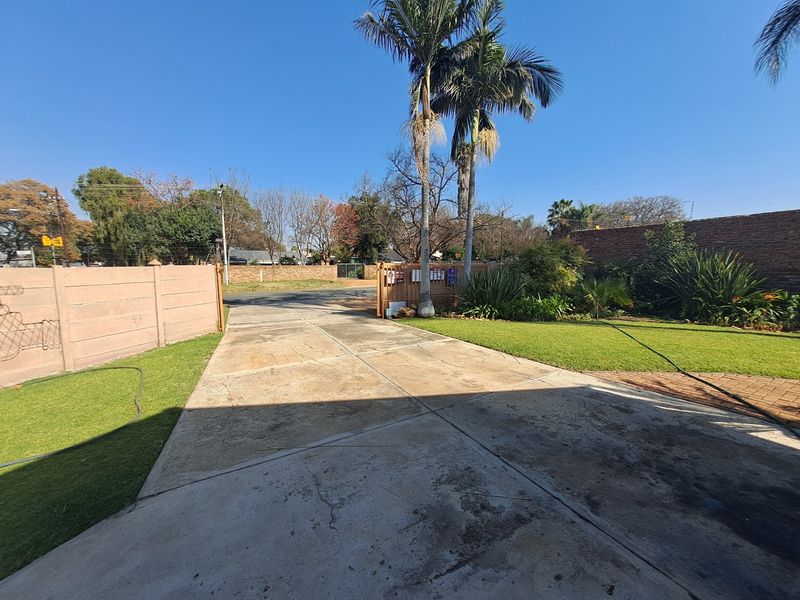 A view of the front driveway featuring a concrete surface, landscaped lawn, and perimeter boundary wall with a wooden gate entrance.
