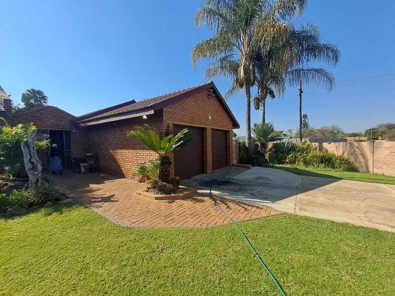 Front view of a brick-faced house featuring a double garage, paved driveway, and established garden area.