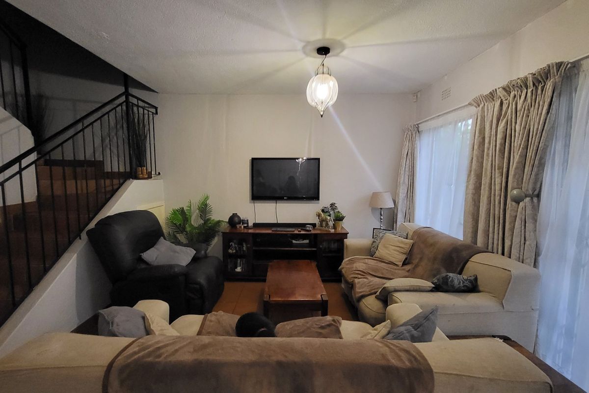 A living room featuring tiled flooring, a staircase with a wrought iron balustrade, and large windows with curtains.